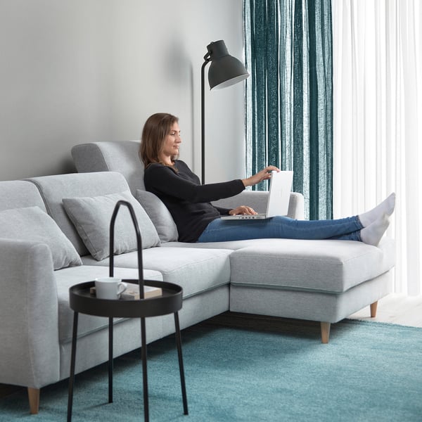 Woman on sofa with laptop by window.