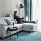 Woman on sofa with laptop by window.