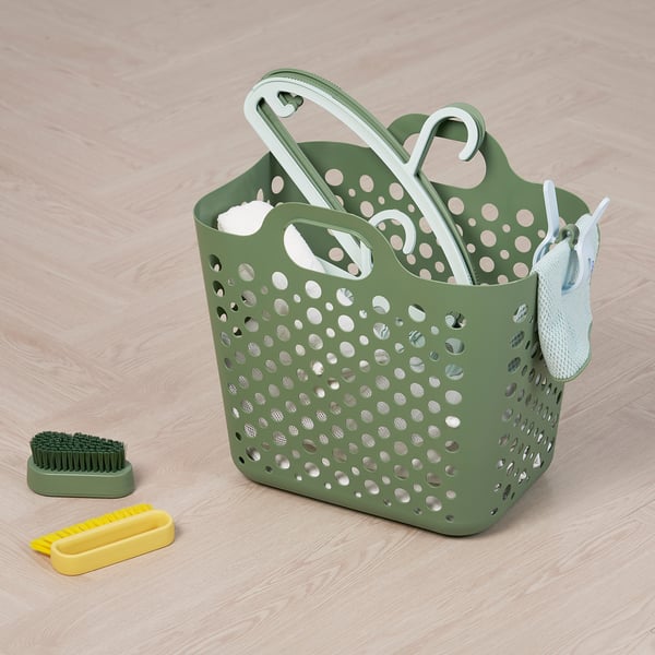 Green perforated laundry basket with white handles, containing cleaning brushes and tools, ideal for organizing and transporting clothes.