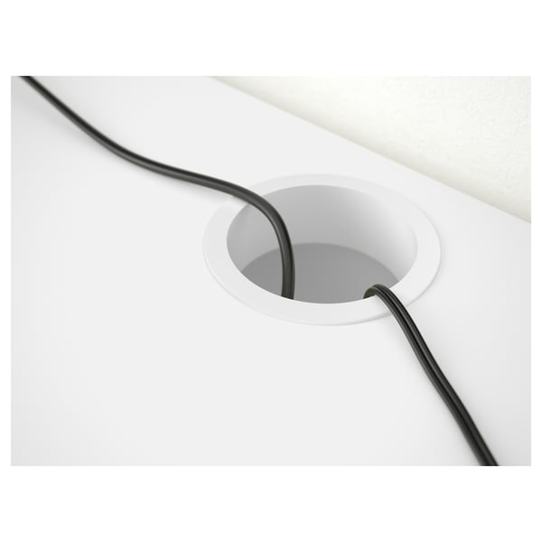 White desk with black cord neatly fed through circular cable hole for organized setup.