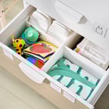 Organized white dresser with baby essentials, including diapers, toys, and dinosaur-patterned clothes.