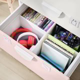 Open white and pink drawers reveal red headphones, video game cases, and notebooks; part of the SMÅSTAD storage collection.