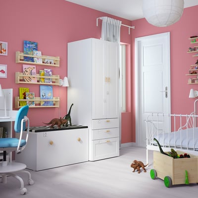 A childrens room with pink walls, white furniture, dinosaur toys, and books.