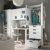 Modern white kids storage unit with wardrobe, drawers, and desk. Colorful decorations and organized clothes.