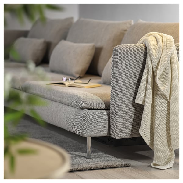 Modern grey fabric sofa bed with cushions and a draped blanket, styled for comfort and relaxation.