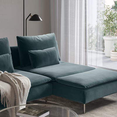 Modern teal sectional sofa with chaise, soft cushions, and a cosy blanket, near a window with plants.