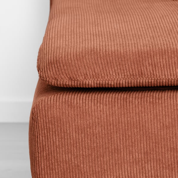 Close-up of a well-cushioned, textured footstool in rust-colored corduroy.