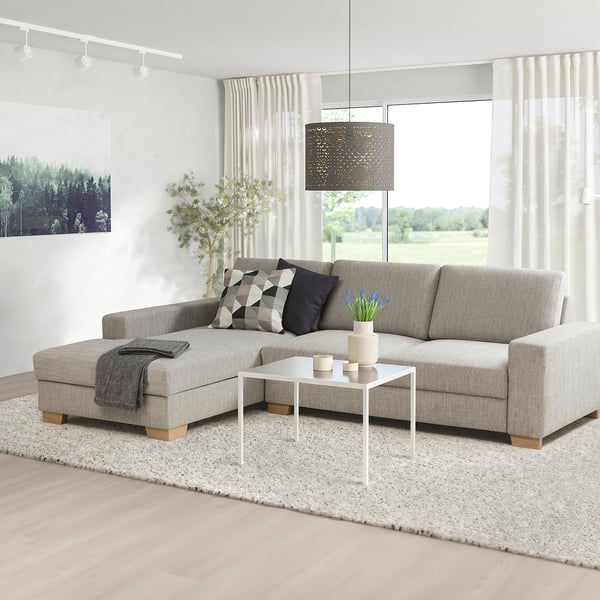Modern living room with gray sofa, pillows, coffee table, plant, rug, and large windows.