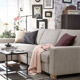 Modern living room with light gray SÖRVALLEN sofa, decorated with cushions and a throw, near a small table with a cup of tea and a book.