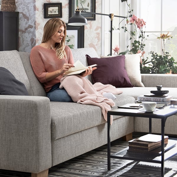 Woman reading on SÖRVALLEN beige sofa, cozy setting with mug and book.