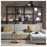 Modern minimalist living room with grey SÖRVALLEN sofa, wooden side table, and black metal shelves decorated with various home decor items.