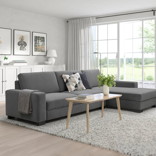 Modern living room with gray sectional sofa, coffee table, and ottoman. Large windows provide natural light, with tasteful decor and a rug.