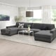 Modern dark grey u-shaped sofa. Large, cosy, minimalist design with pillows and blanket. Centred on light rug, near window with curtains.