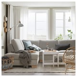 Modern living room a gray l-shaped sofa with a white coffee table. Large window with sheer curtains lets in natural light.