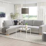 Modern living room with a grey SÖRVALLEN sectional sofa, square white coffee table, patterned throw pillows, and a large window with sheer curtains.