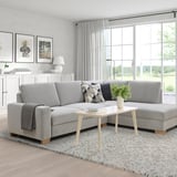 Modern living room with SÖRVALLEN gray sofa, large windows. Light wood coffee table, white curtains. Minimalist design.