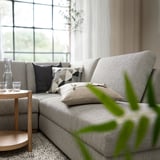 Modern gray SÖRVALLEN sofa, minimalist design with black and white pillows, wooden side table, and green plant, near large window.