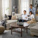 Three people chat on beige SÖRVALLEN sofa. Coffee table with bowl and plant in front of large window.