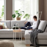 Woman reading on grey SÖRVALLEN sofa by window with mug and plants.