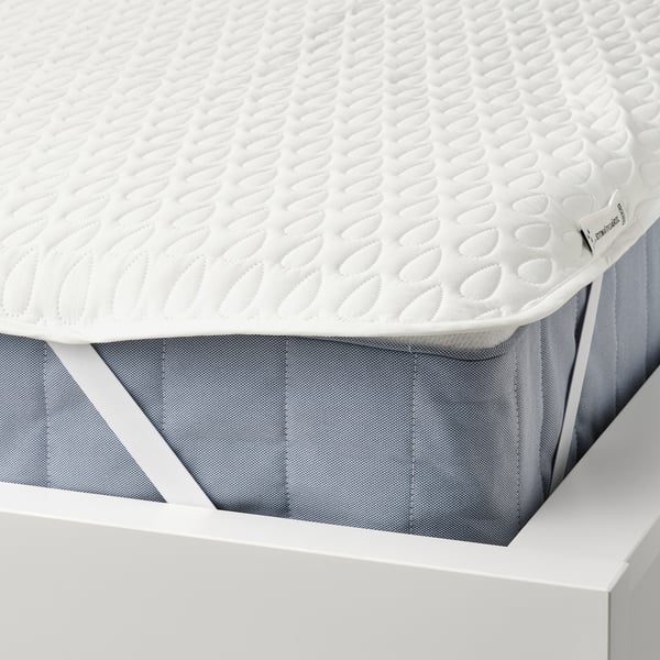 White mattress protector on a bed. It has a soft wadding surface and is waterproof inside. Elastic straps keep it secure.