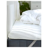 White mattress protector on bed with wadding, waterproof layer, elastic straps for fit.