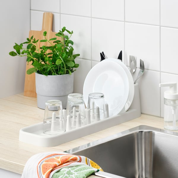 Kitchen sink with STÄMLING dish drainer holding plates, glasses, and cutlery, beside a plant and soap dispenser.
