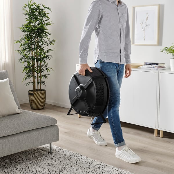 Person carrying black air purifier with handle in modern living room. Product: STARKVIND.