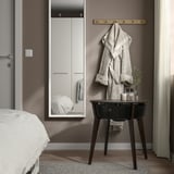 Modern bedroom with STARKVIND air purifier table near bed. Table holds towels and small items. White walls and curtains frame scene.