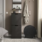 Black air purifier, round and modern, fits neatly between cabinet and window, with a smooth surface and sleek legs.