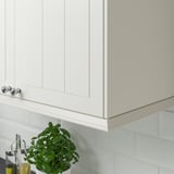 White kitchen cabinet with silver knobs, green plant, under-cabinet lighting.