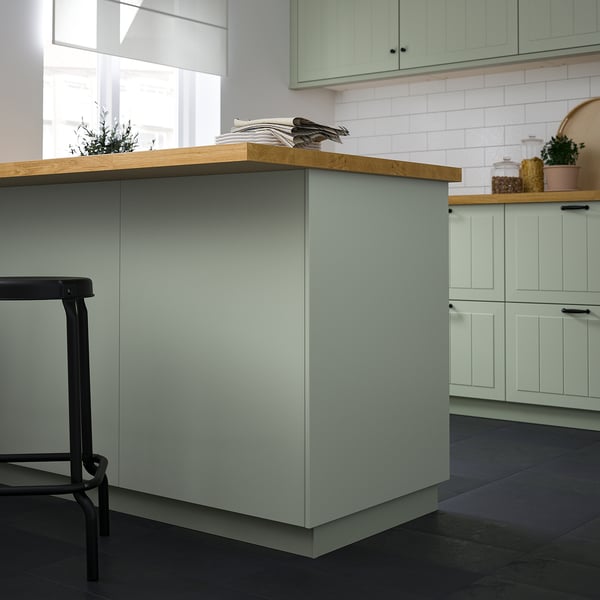 Modern kitchen with green panel, butcher block counter, stool & plant.