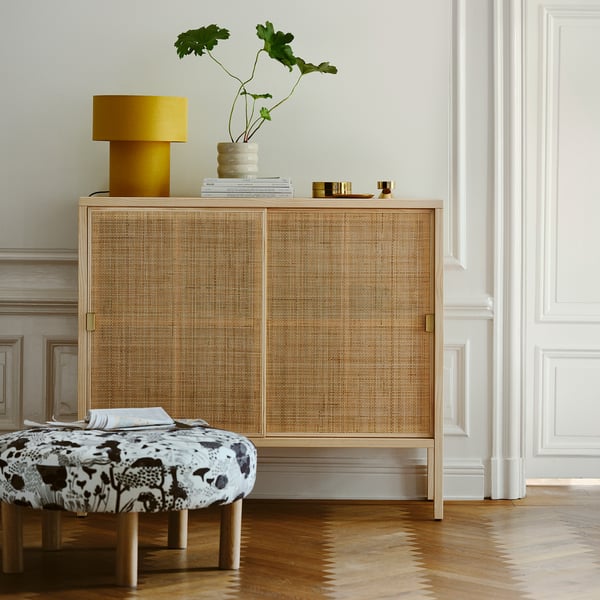 Scandinavian rattan cabinet with brass handles, lamp, vase, books, & bench - cozy interior