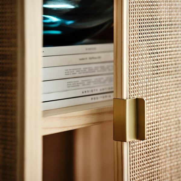 Closed white rattan cabinet with gold handles, showing part of neatly stacked books.