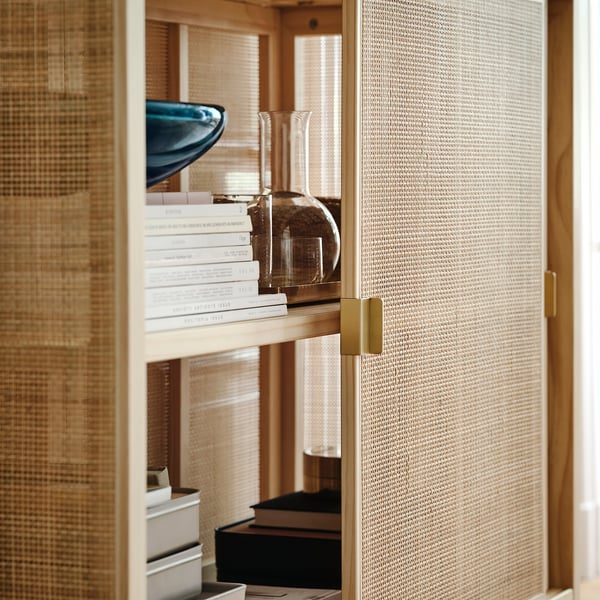 Rattan cabinet with adjustable feet, sliding doors, brass handles, holding books and vases.