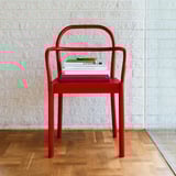 Red STOCKHOLM 2025 chair against white brick wall, holding books, slim & sleek design, wooden floor.