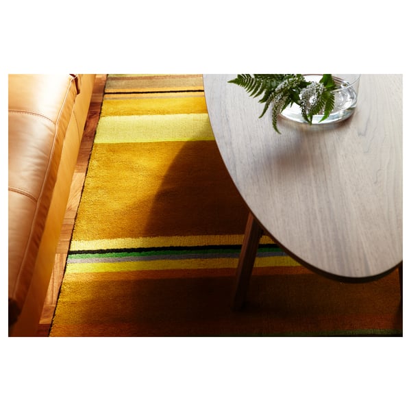 Coffee table with wooden top and metal legs on striped rug, featuring a vase with greenery.