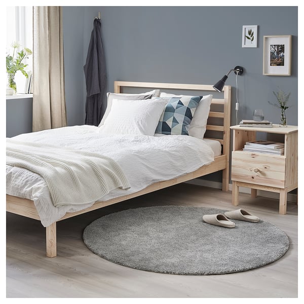 Minimalist bedroom with white bedding, grey rug, wooden furniture, and blue walls. A cozy, modern design.