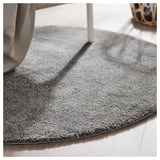 Gray circular rug with a thick, soft pile lies on a wooden floor, partially under a striped chair.