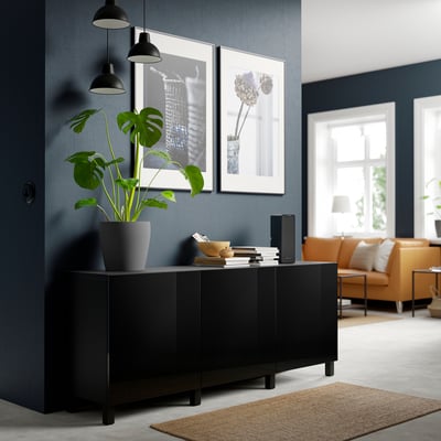 Modern room with black STUBBARP legs under sideboard, holding plant, framed art, and books. Orange leather chair and beige rug nearby.