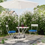 Small outdoor setup with white foldable table and chairs, blue cushions, white flowers, and a drink pitcher under a white umbrella.