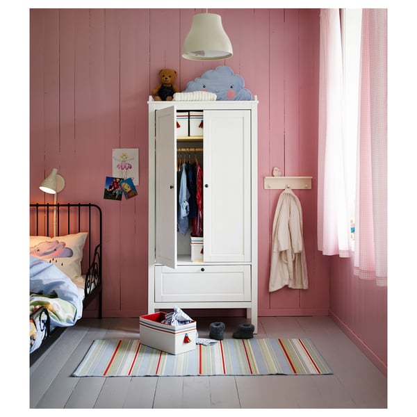 Childs room with white SUNDVIK wardrobe, bear, clothes, rug, pink walls, black bed, lamp, posters, and curtain.