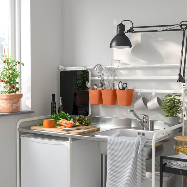 Modern kitchen with white sink, black lamp, orange containers, plants, gray towel.