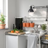 Modern kitchen with white sink, black lamp, orange containers, plants, gray towel.