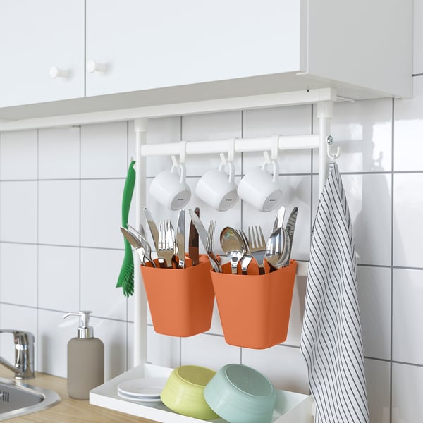 Kitchen organizer system. Utensils in hanging pots, mugs, green towel, dishes.