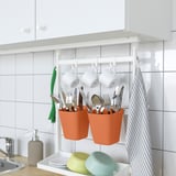 Kitchen organizer system. Utensils in hanging pots, mugs, green towel, dishes.