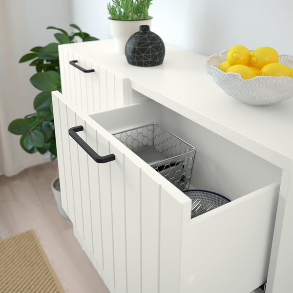 White storage cabinet with open door revealing mesh basket inside, lemons in bowl on top.
