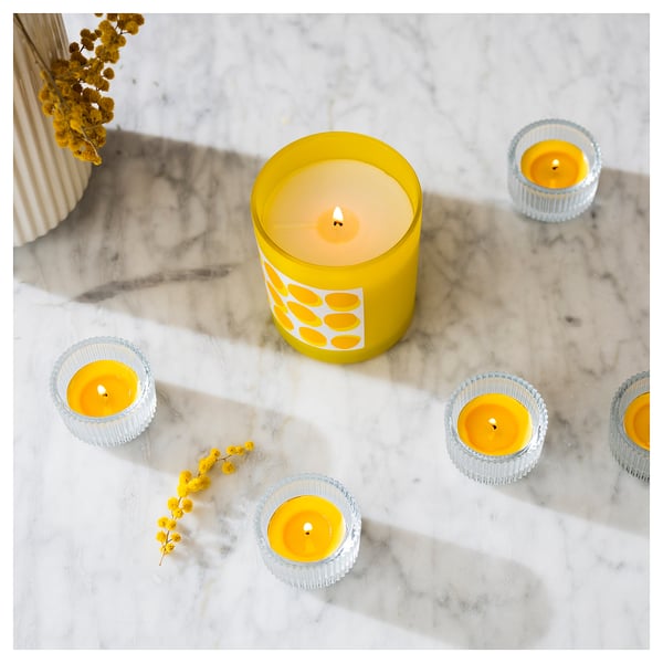 Six yellow candles on marble with yellow flowers.