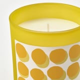 Bright yellow scented candle with orange polka dots in a glass jar, lit and emitting a warm glow.