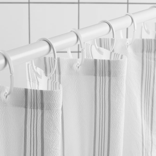 White shower curtain with grey stripes hangs on rings. Dense weave for water repellence, soft, wavy seersucker texture.