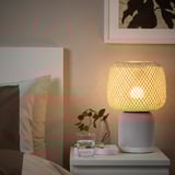 SYMFONISK lamp with woven shade on bedside, water, plant, cushions, picture.